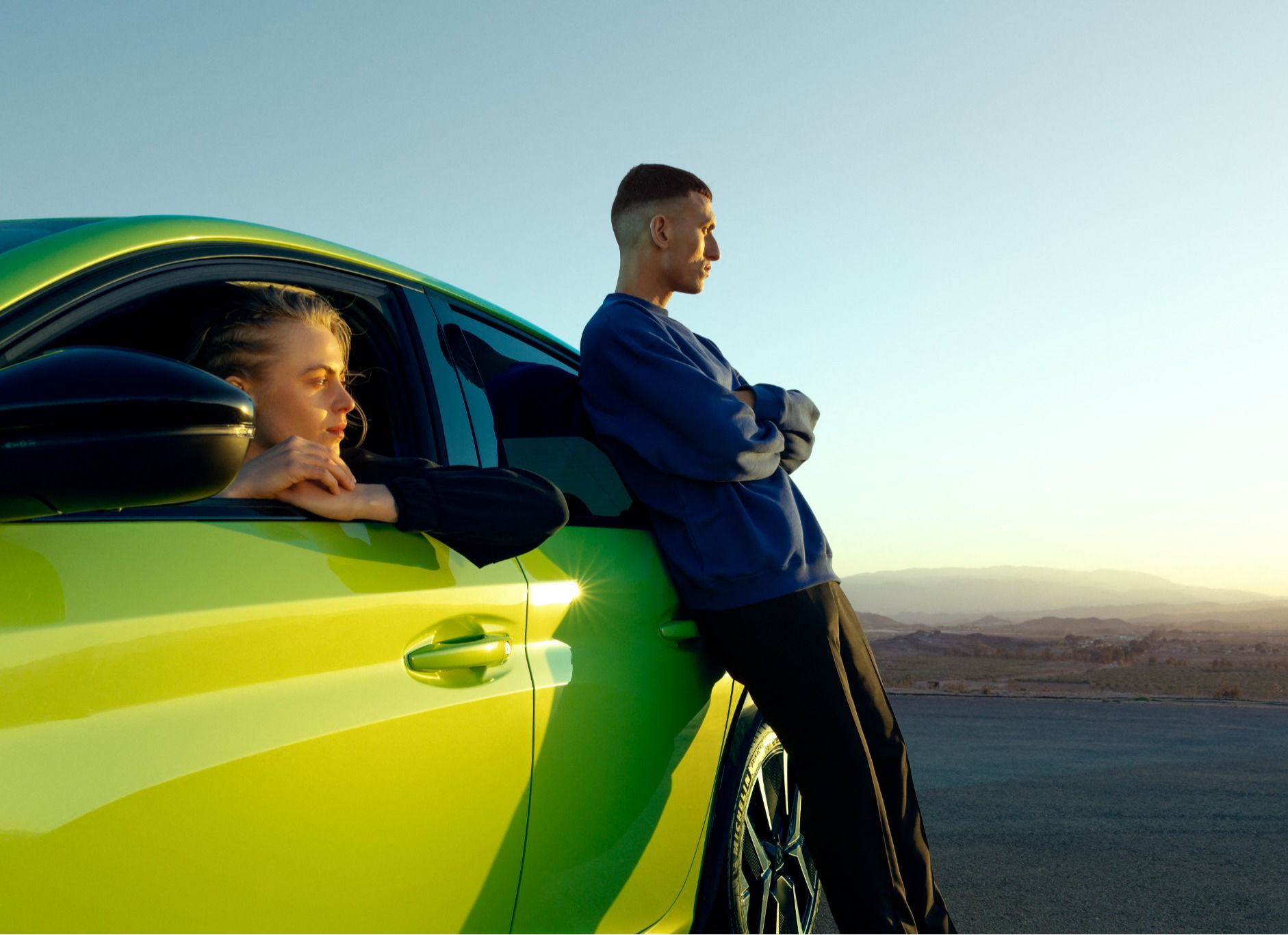 Green Peugeot 2008-e with a woman seating in the driver seat and a man standing on the side of the vehicle