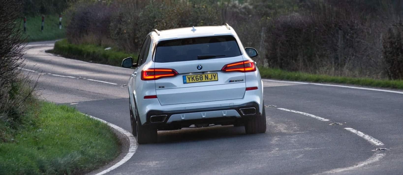 BMW X5 White BMW X5 driving down road back view