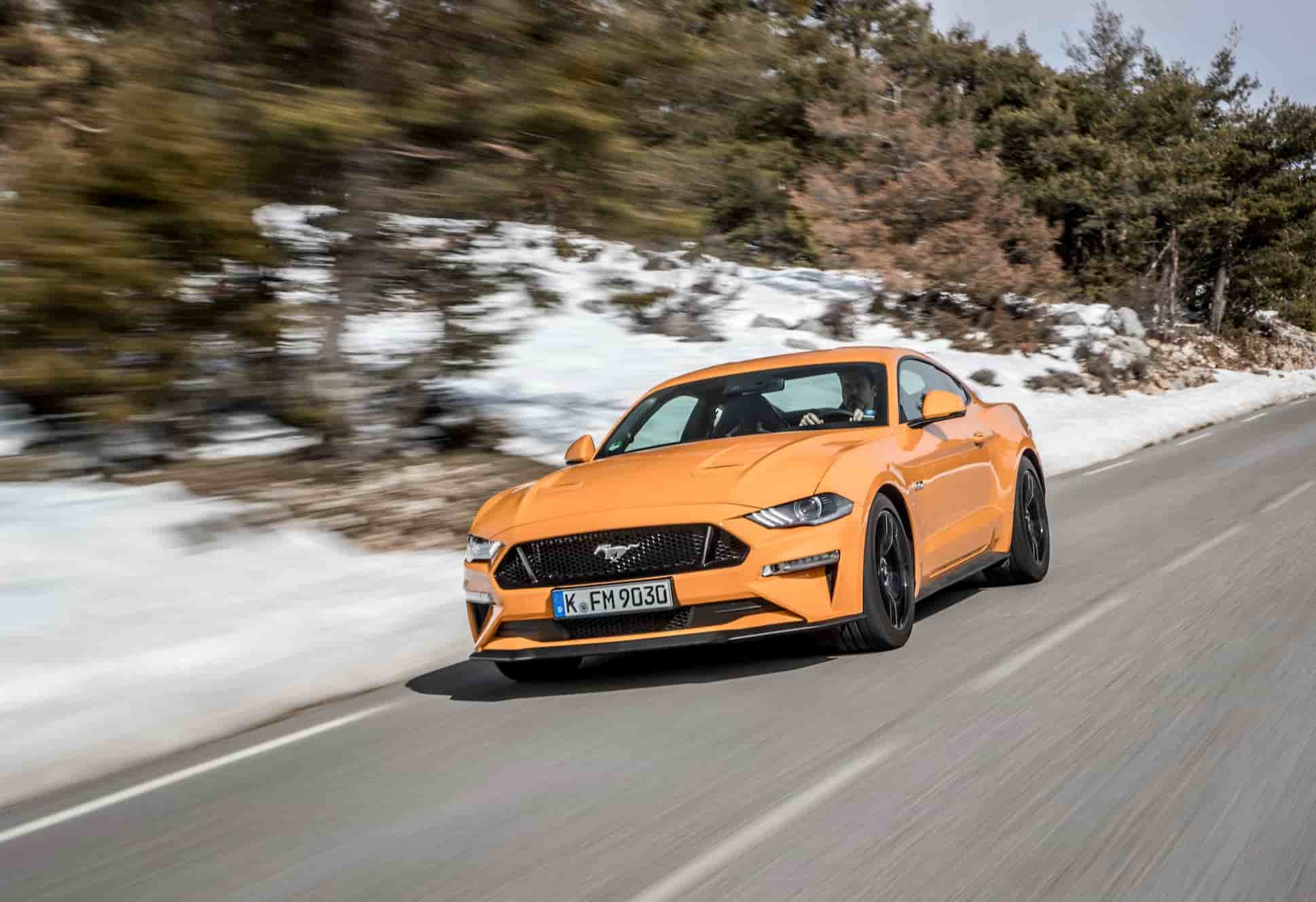 Orange ford mustang driving on snowy road