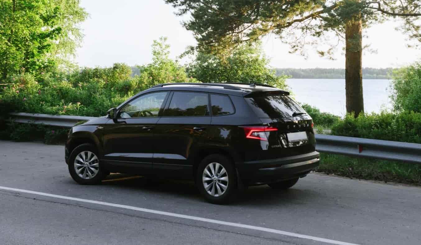 black skoda driving down a road with trees and water in the background