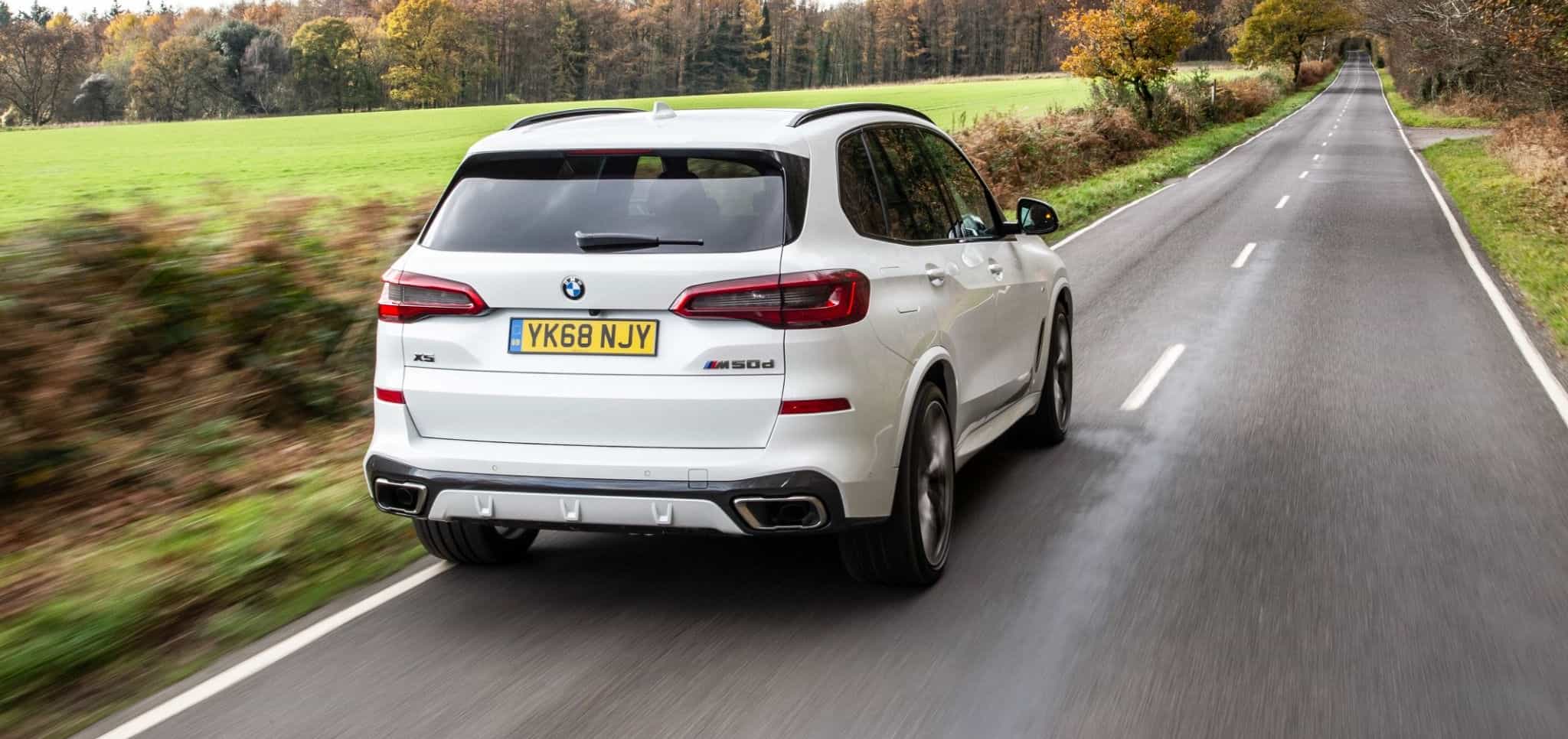 rear view white bmw x5 driving along country road