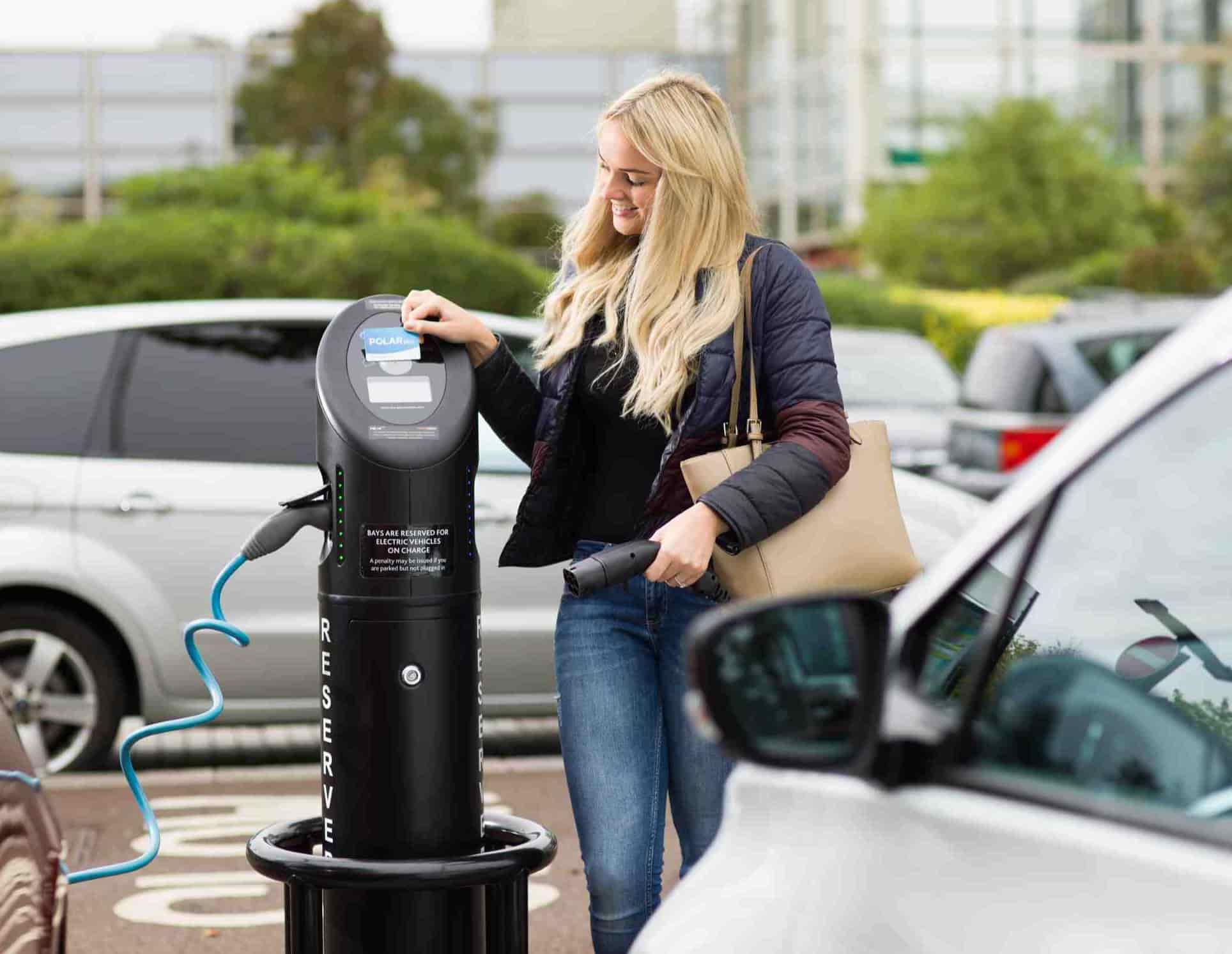 woman standing next to an electric car charger in use