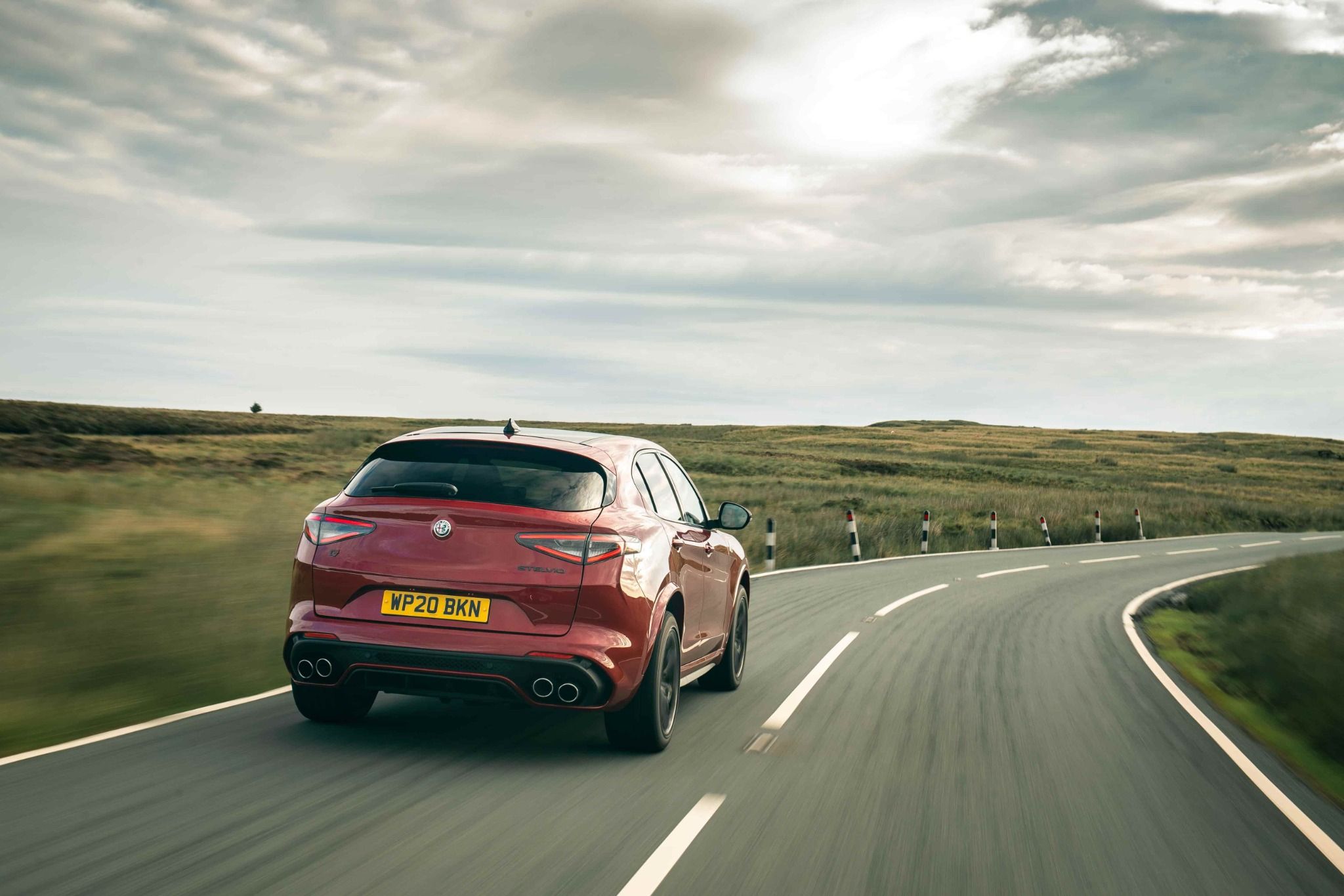 back of red alfa romeo driving down a country road