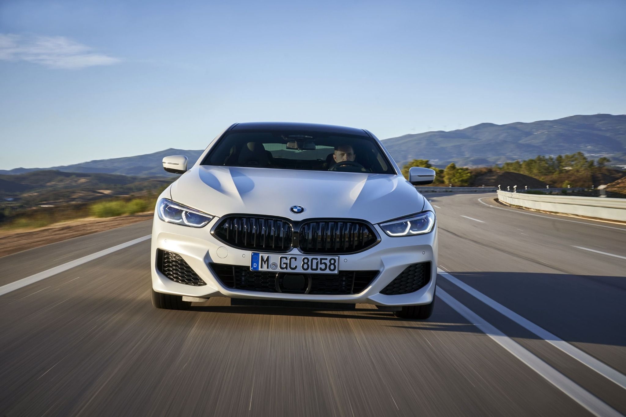 front view of white bmw 8 series driving down a road