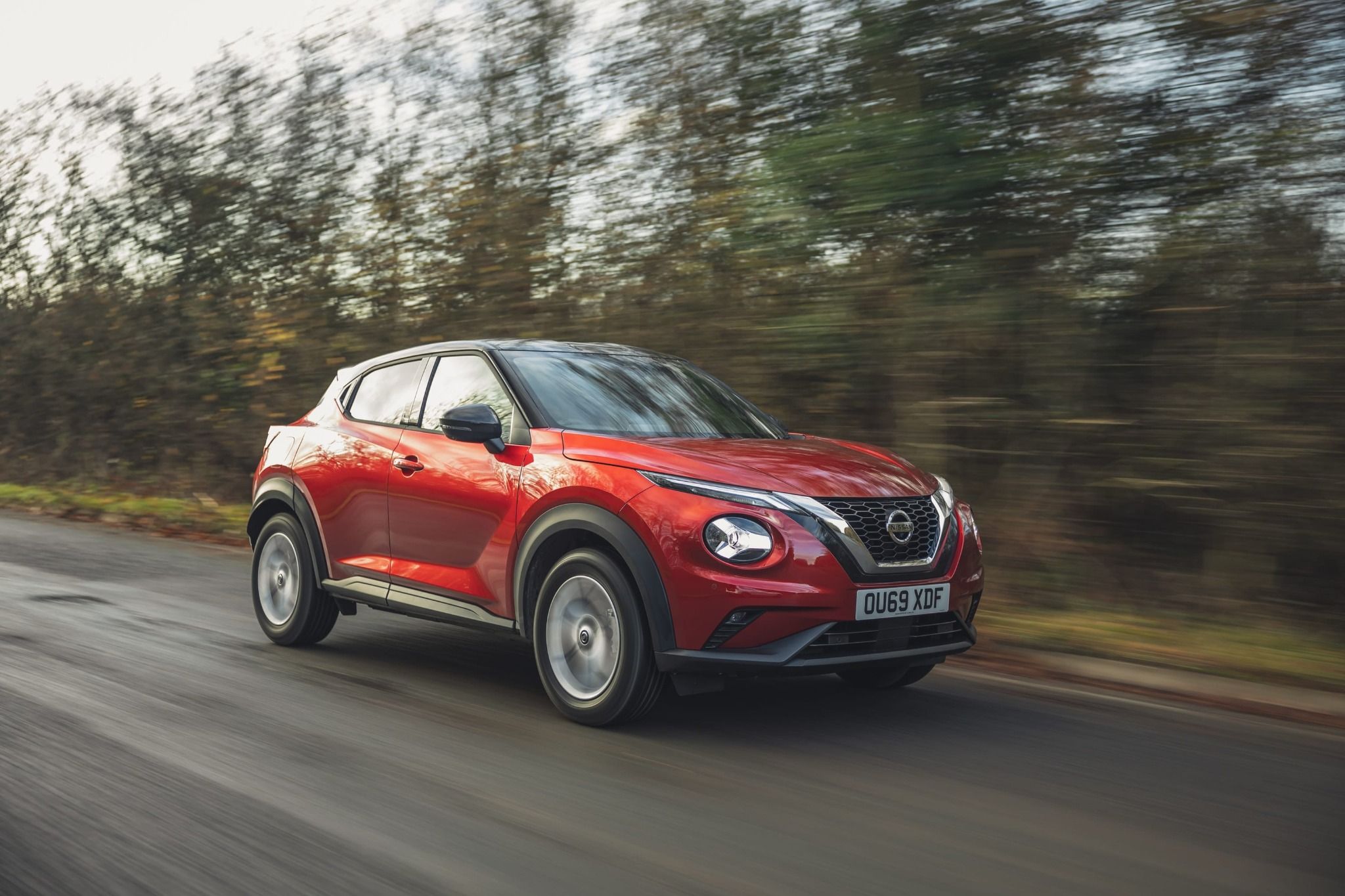 side view of red nissan juke driving down a road