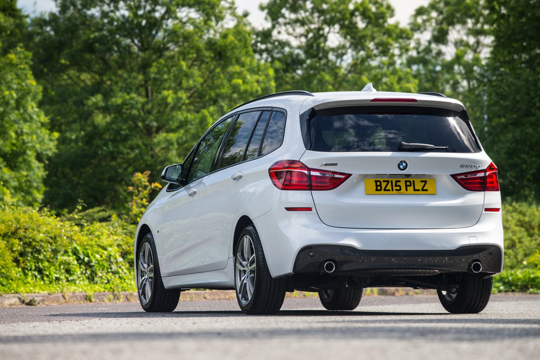 White BMW Photographed from the Rear Driving Along a Road Surrounded by Trees