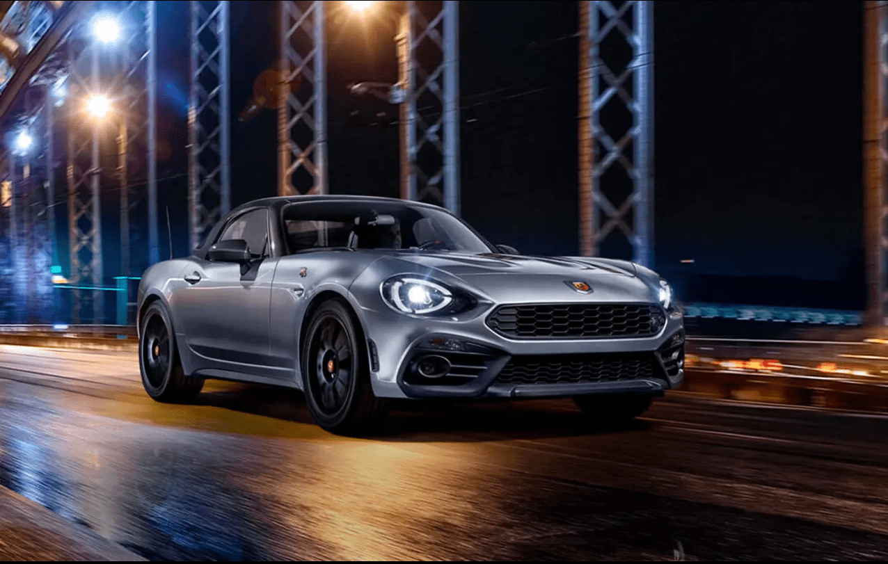 silver front view abarth 124 gt driving down a city road at night