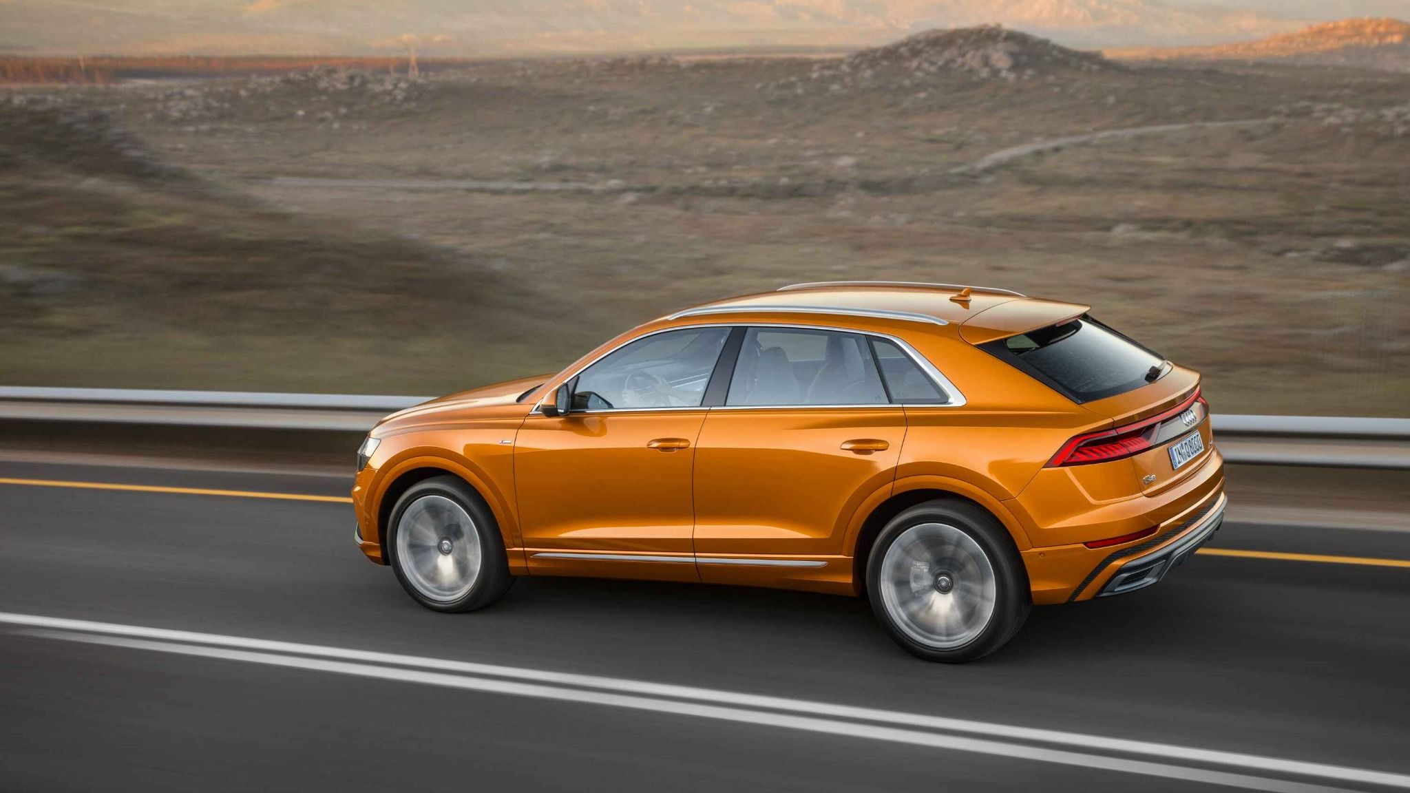 side view of orange audi q8 driving down a road
