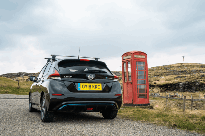 Rear view of a black nissan leaf parked next to a red telephone box an surrounded by grass
