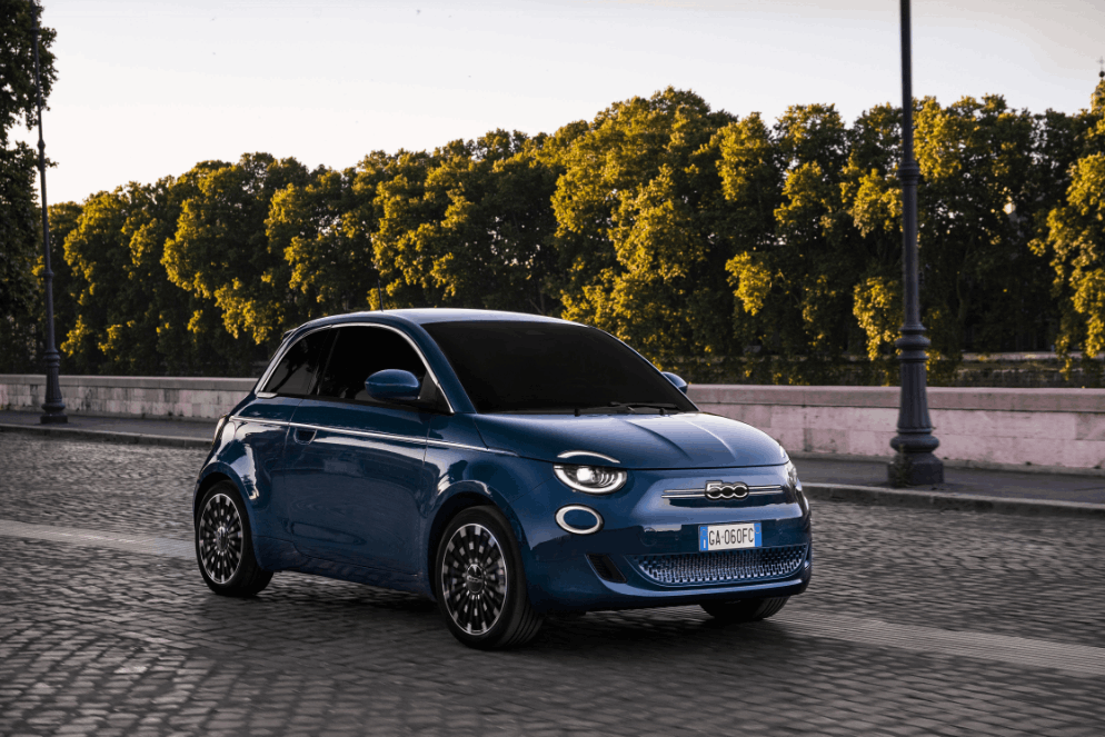 blue fiat 500 driving down a street with trees in the back