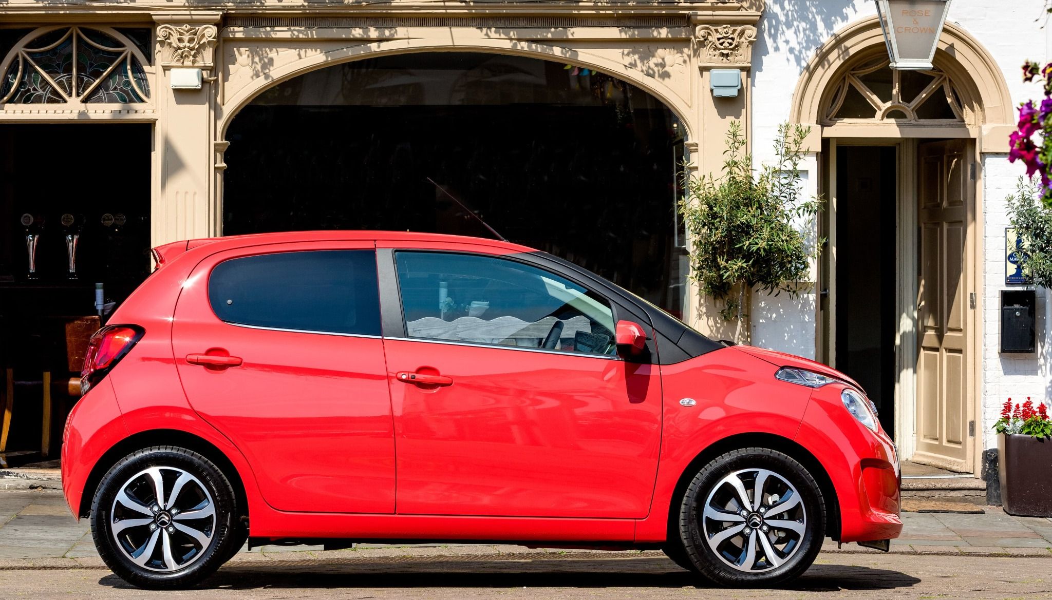 side of red citroen c1 in front of a building