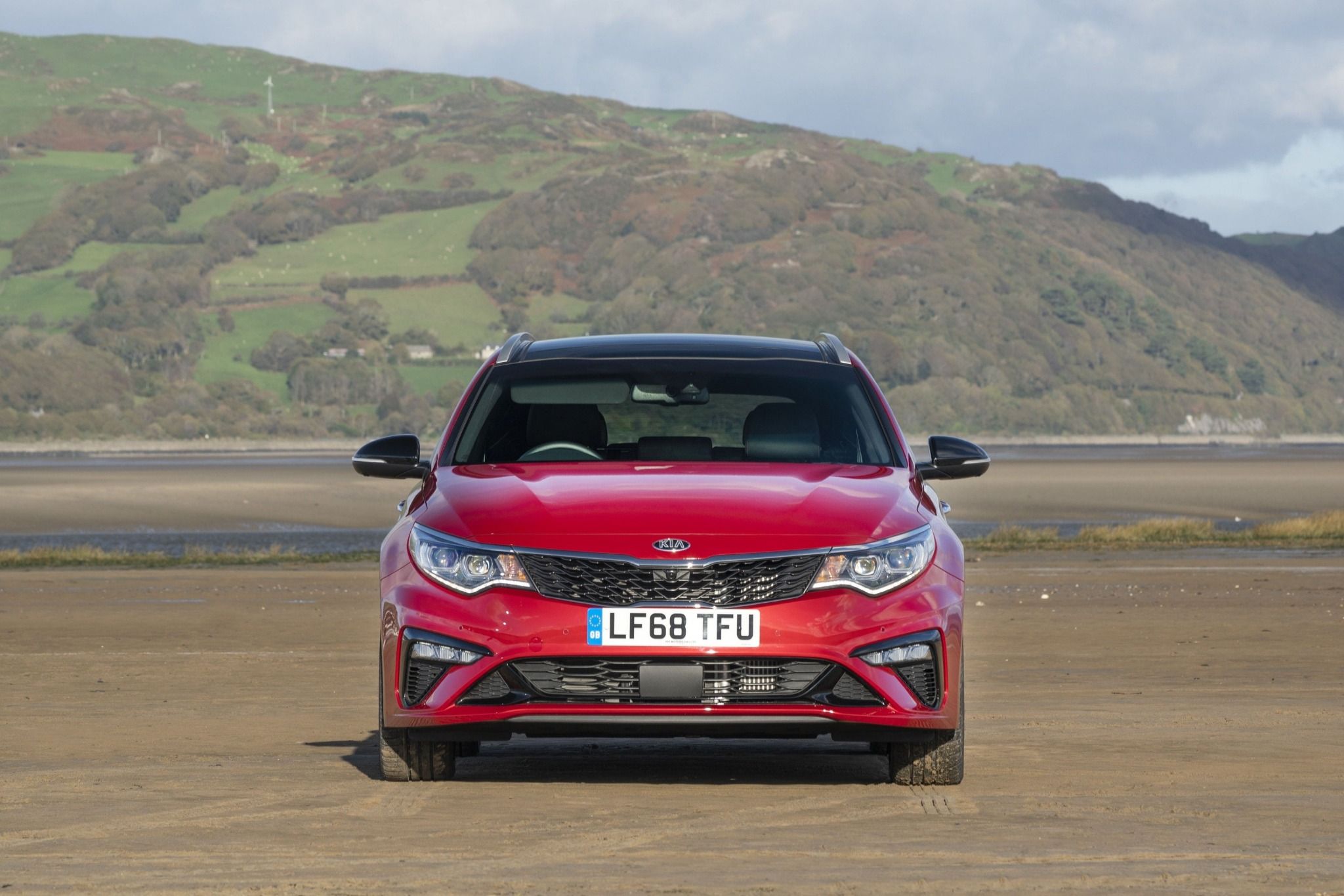Front of red Kia Optima parked in front of a hill