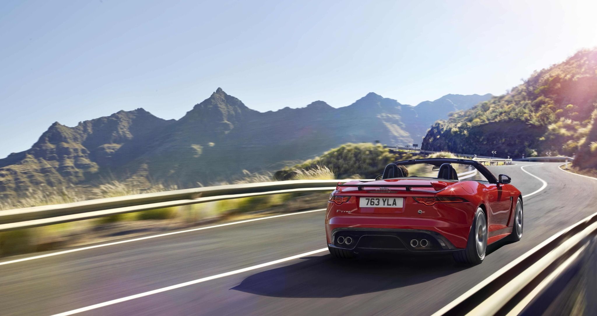 red jaguar f type convertible driving down a road with mountains in the background