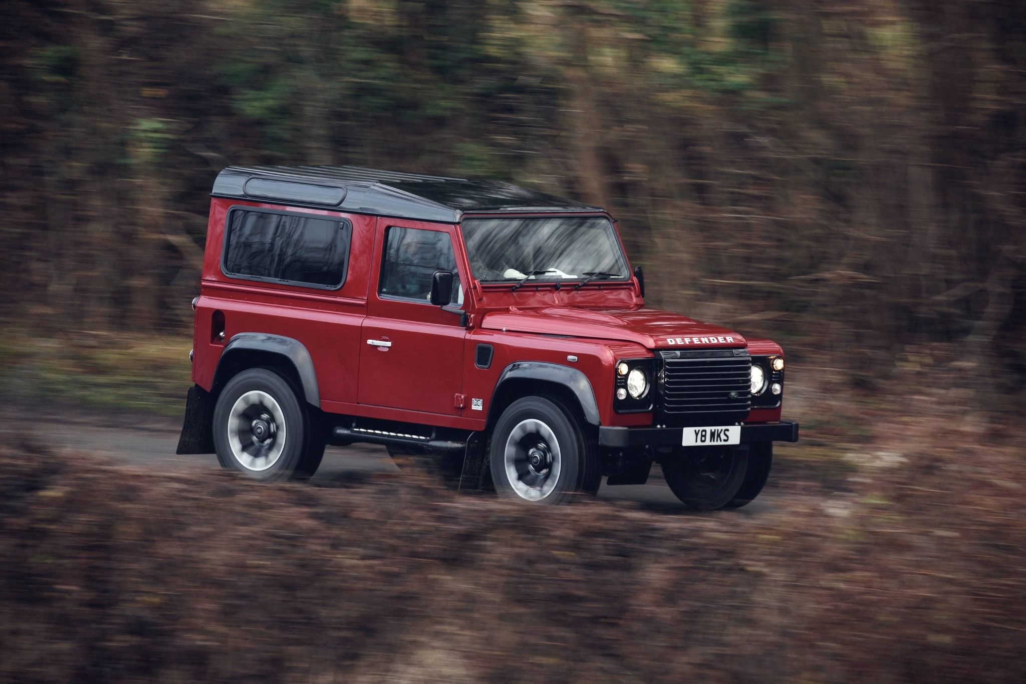 red land rover defender driving through trees side view