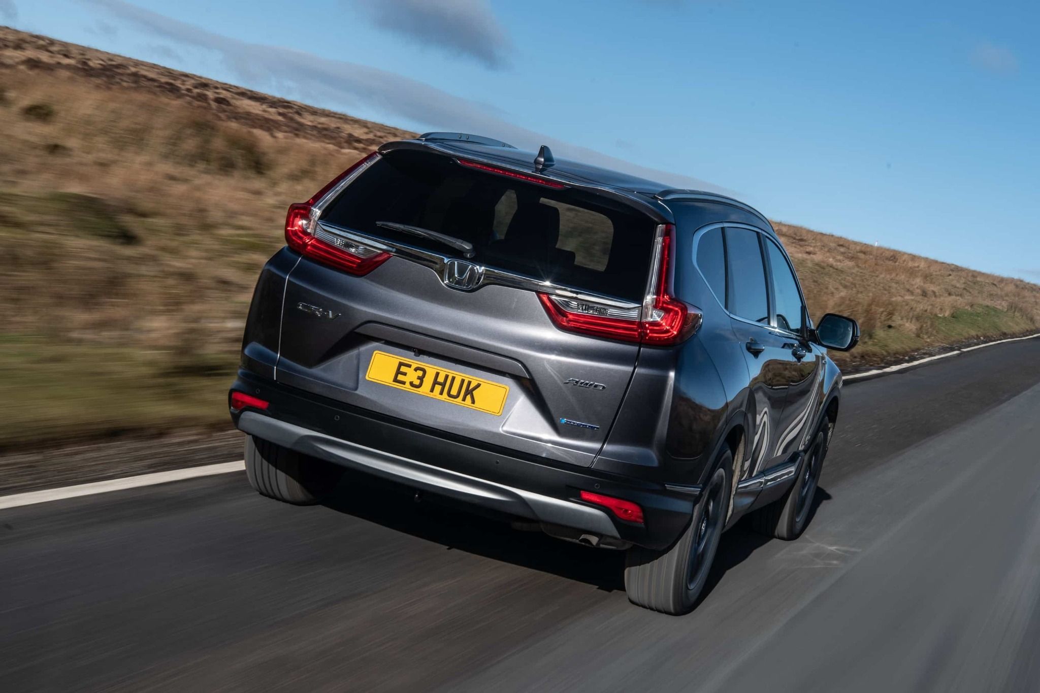 rear view of silver honda cr v hybrid driving down a country road