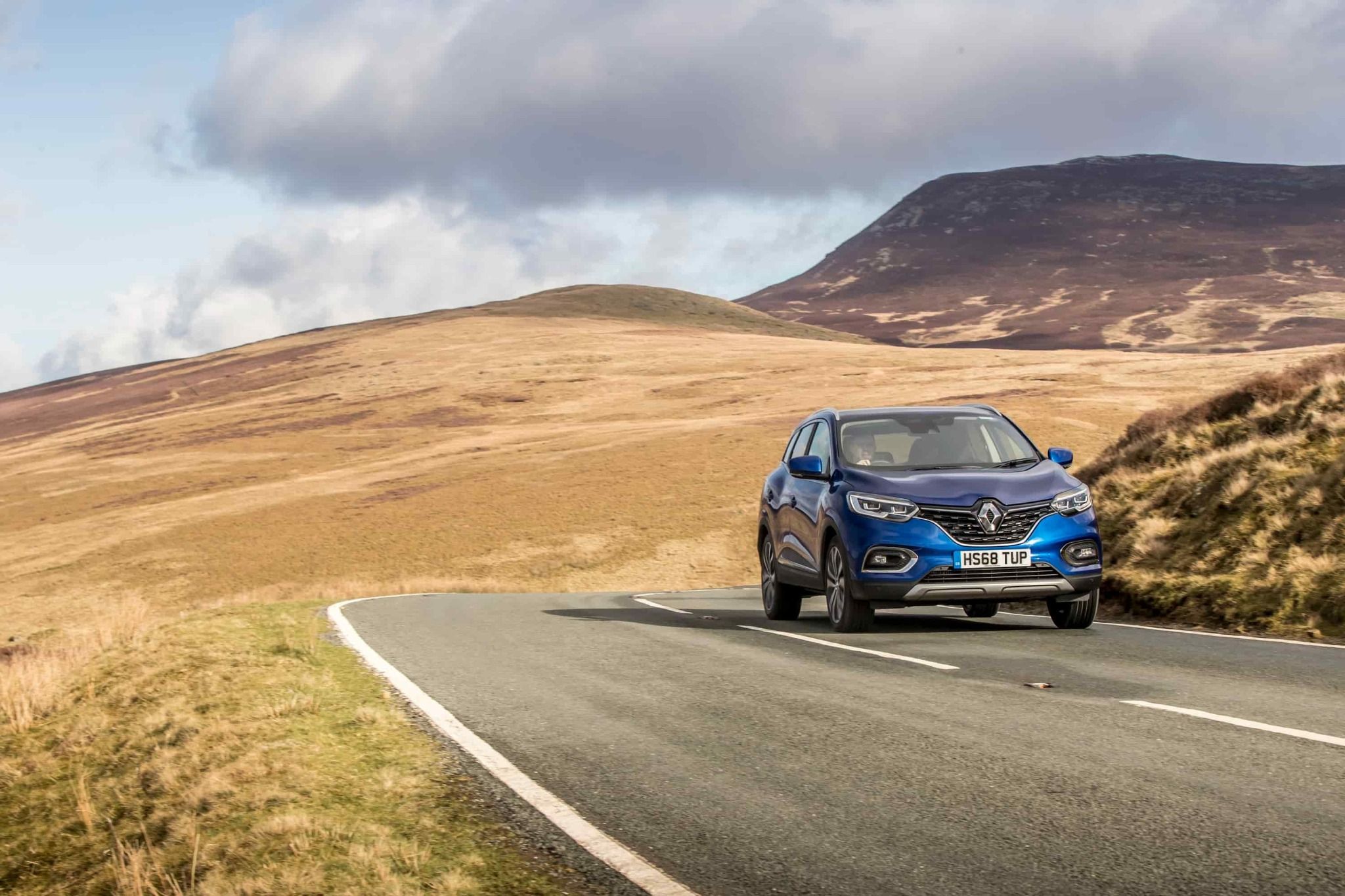 blue renault kadjar driving on a country road with hills in the background