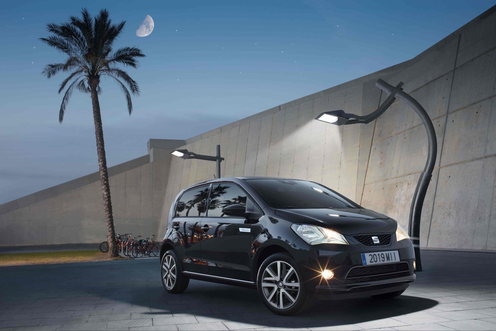 seat mii in black parked outside with lights a palm tree and the moon in the background