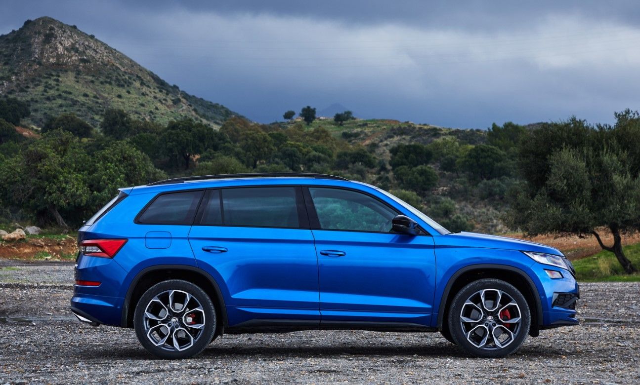 side view of a blue Skoda Kodiaq on a gravel path and with mountains in the background