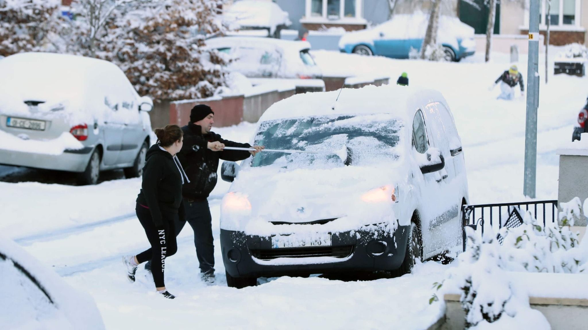 Man and Woman Brushing Snow Off Their Van in the Street