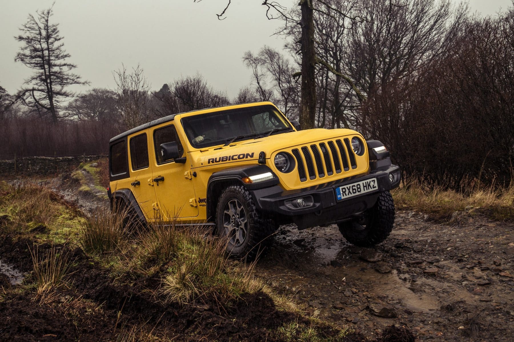 Yellow Jeep Wrangler driving on muddy track