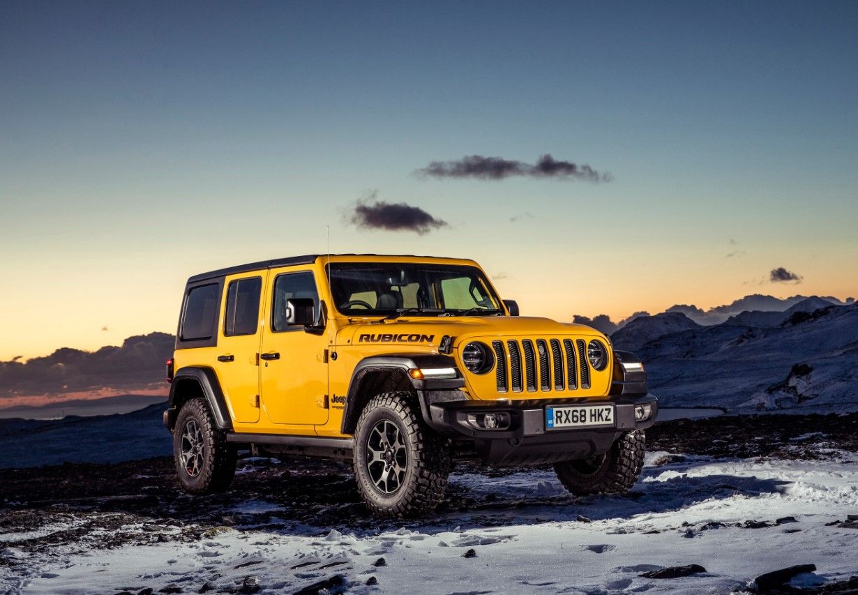 Yellow Jeep Wrangler sitting on a snowy mountain in front of a sunset