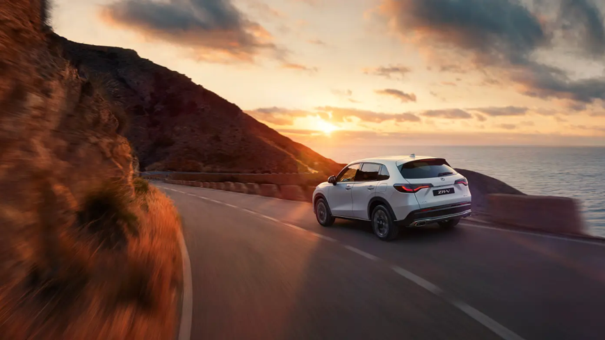 All-New Honda ZR-V driving on a mountain road at sunset.