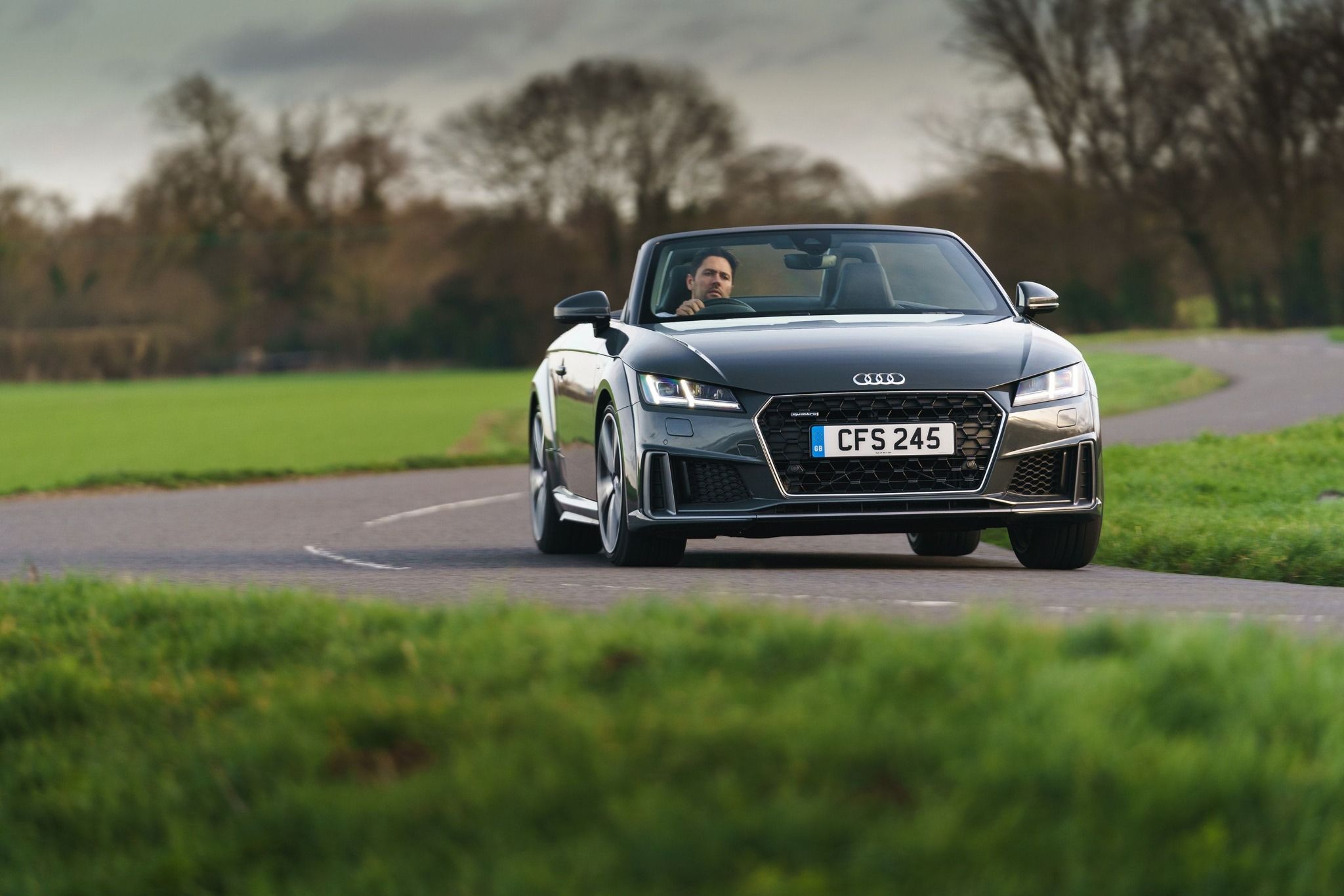 front view of a grey audi tt roadster cabriolet with the roof down and driving on a road