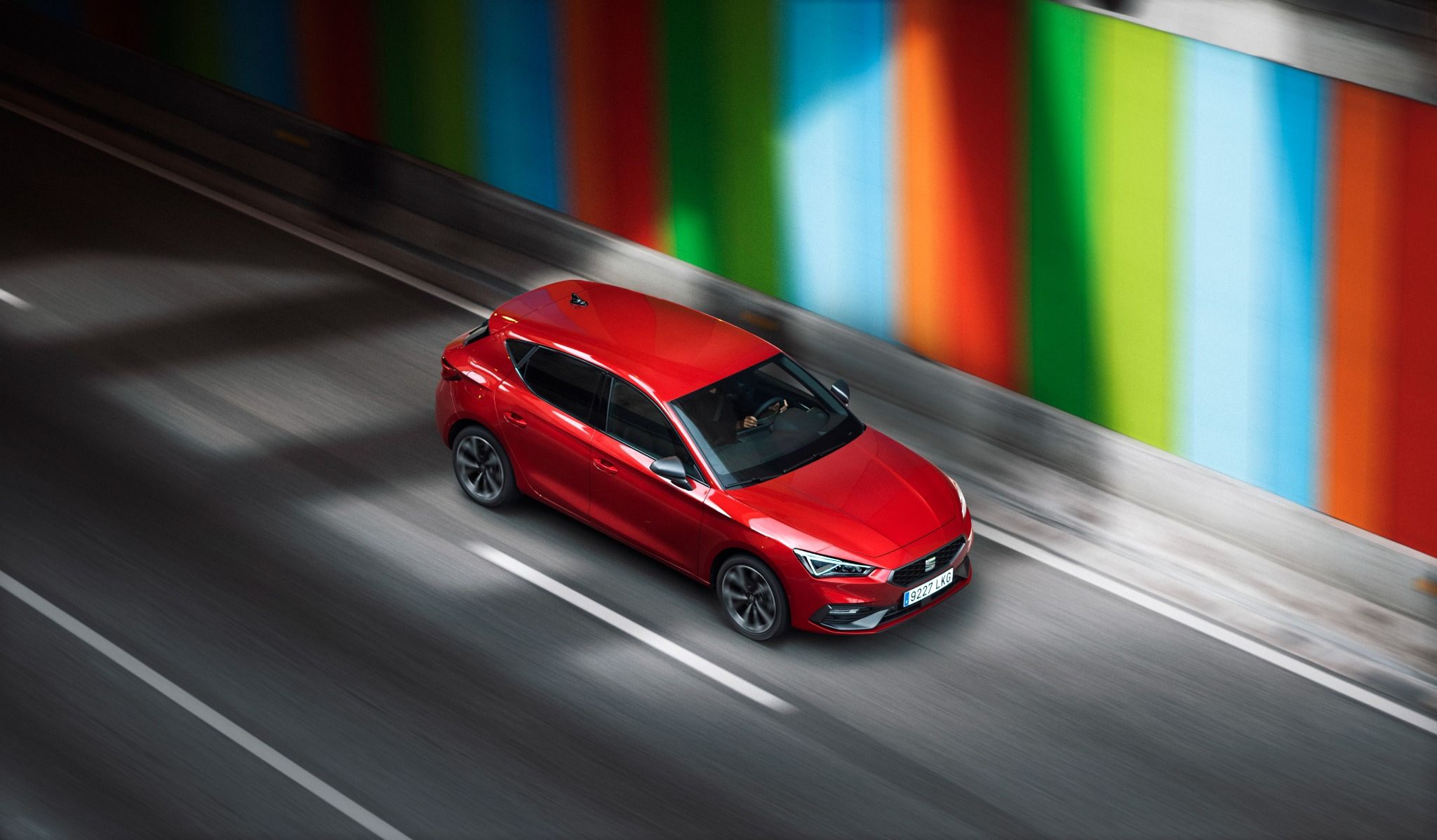 Seat Leon hybrid in red driving next to rainbow wall