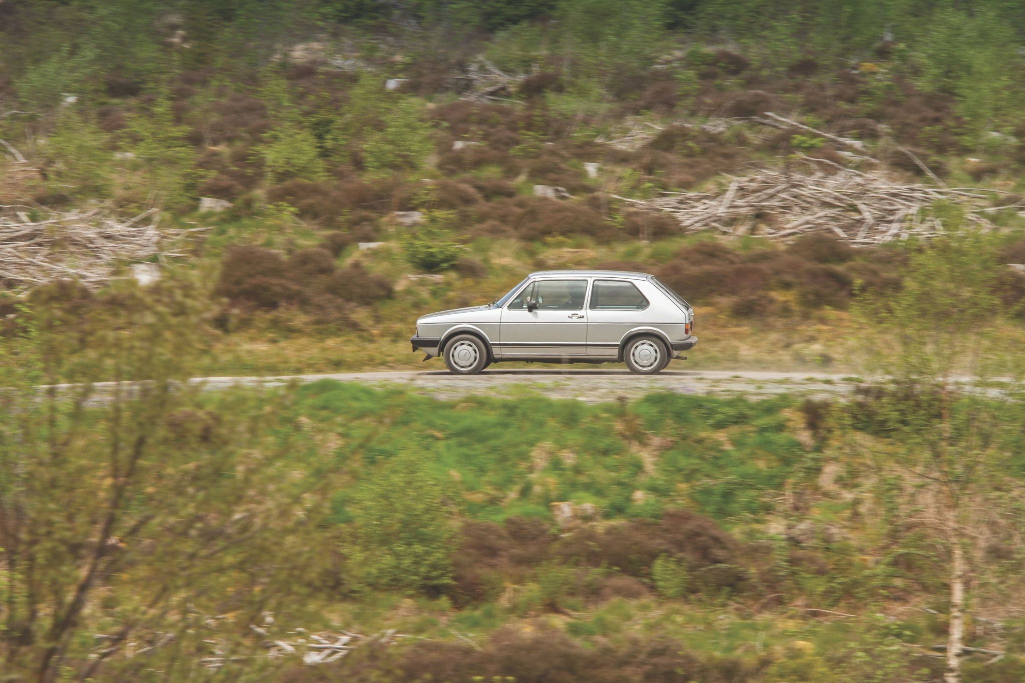 Side view of an MK1 Volkswagen Golf GTI driving on a road with grass either side