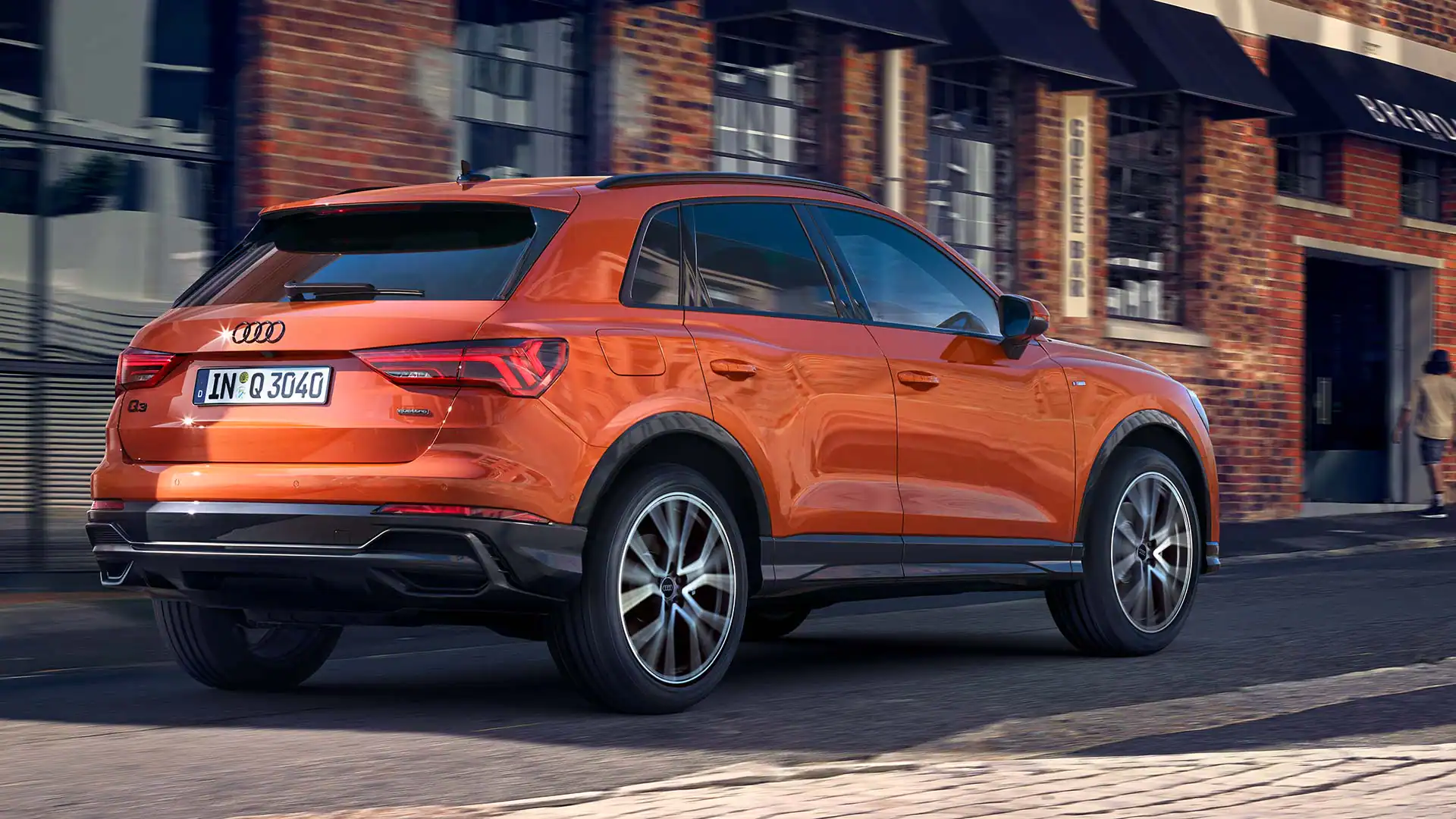exterior rear side view of an orange audi q3 rear driving down a city road