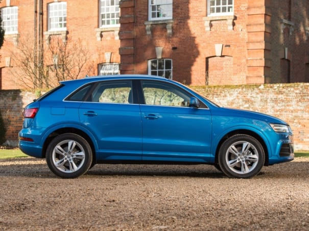side exterior view of a blue audi q3 parked up next to a brick building with lots of windows