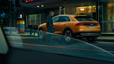 Orange Audi Q8 rear side parked with man getting in