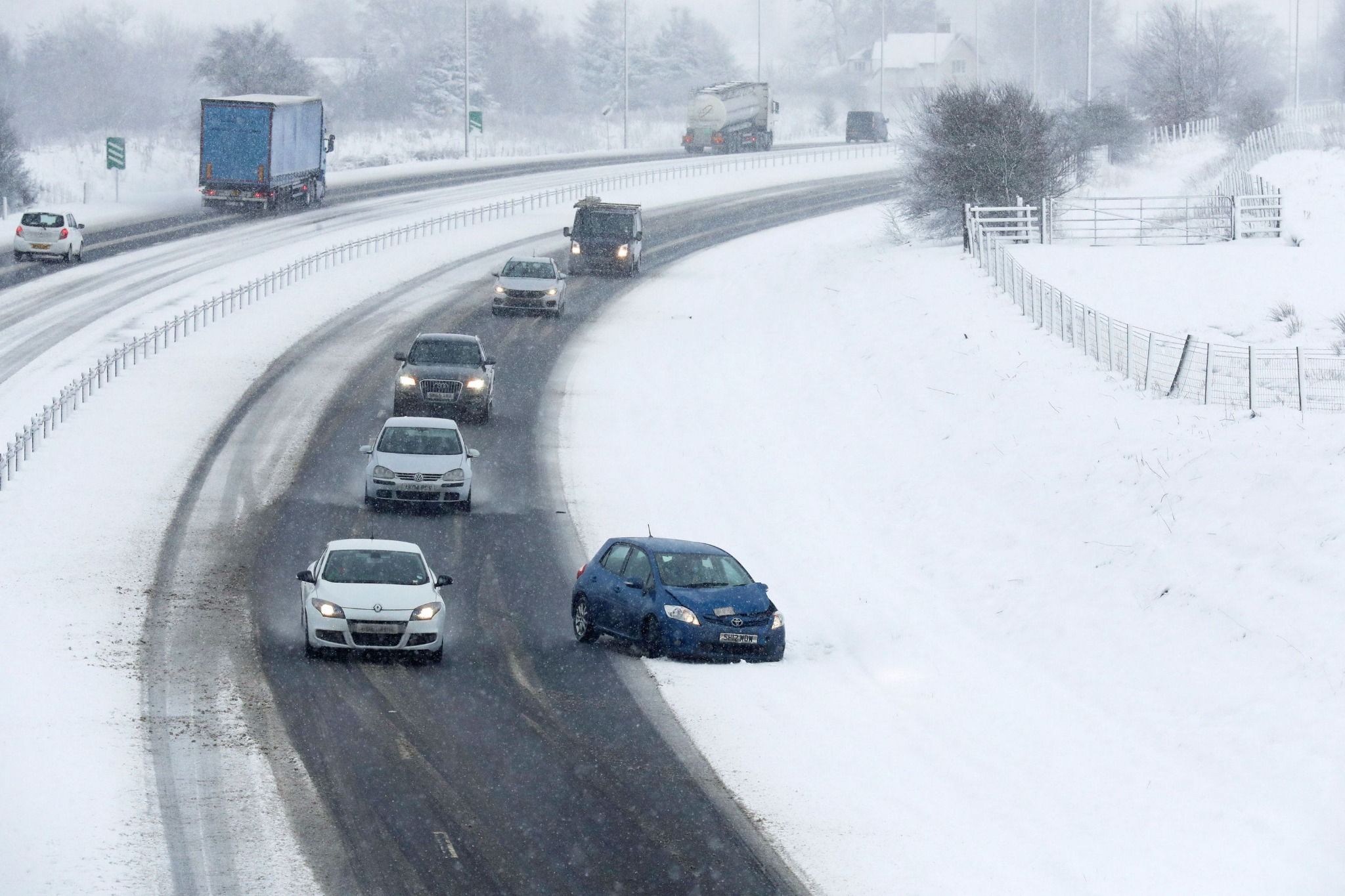 cars driving on a main road and a blue car has spun off the road in the snow