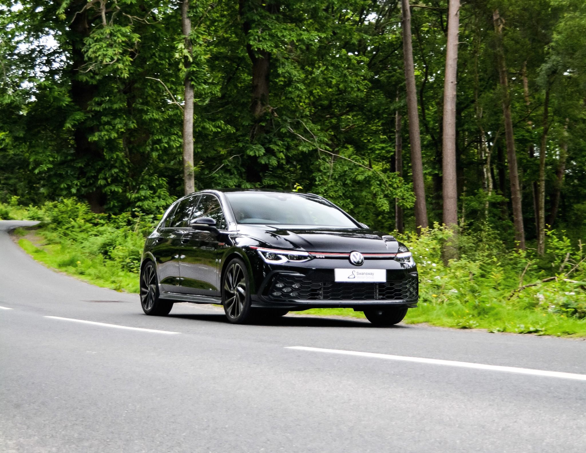 Black Golf GTI driving on road in a wooded area