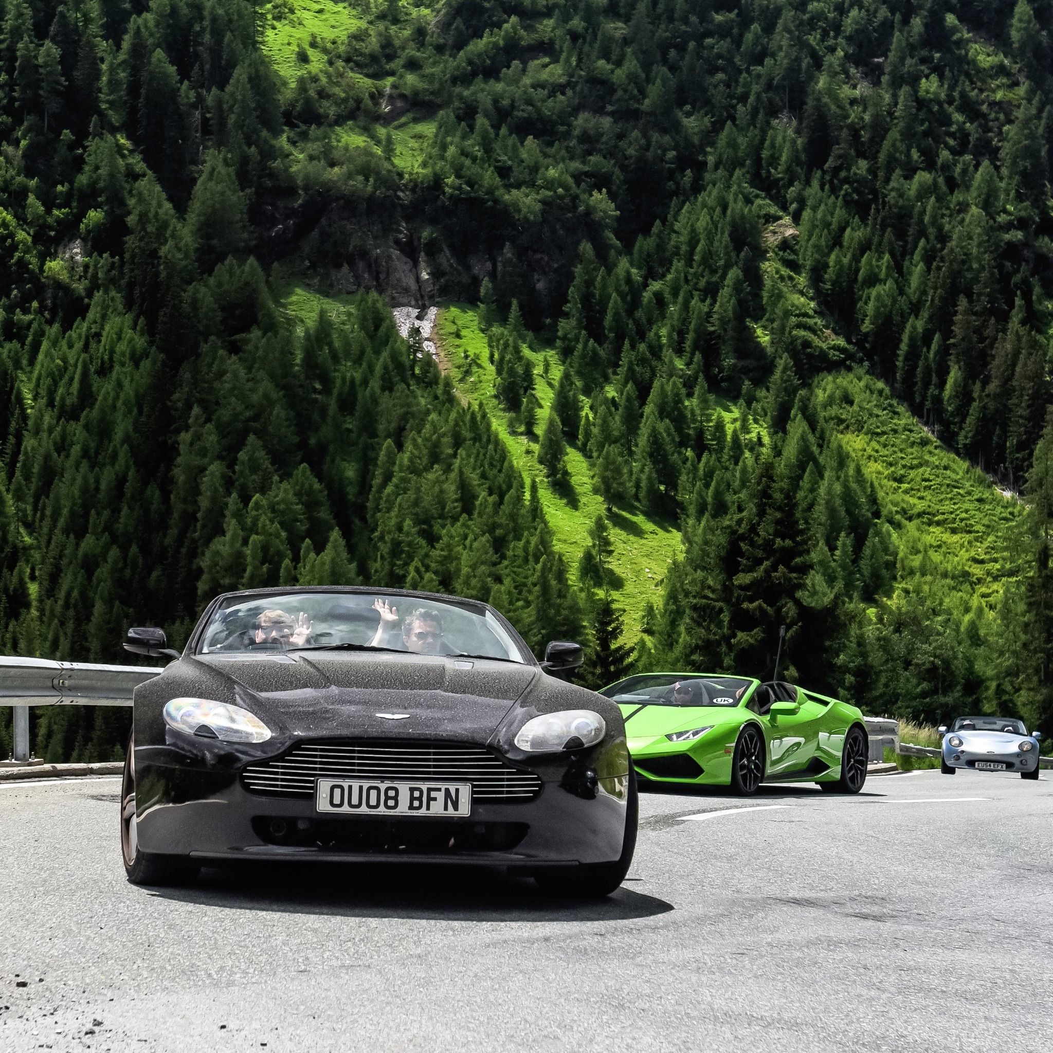 Black Aston martin driving on a road with couple waving