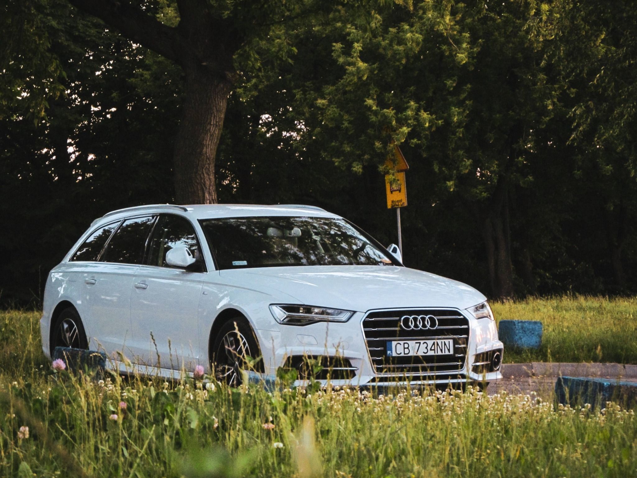 white audi a6 allroad driving down a road surrounded by trees