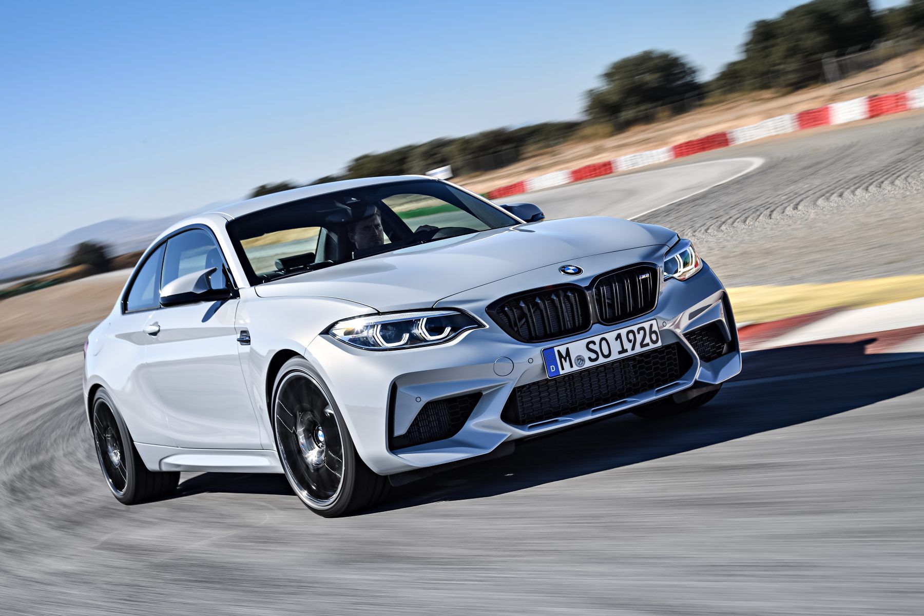 Front view of a white BMW M2 Competition driving on a track
