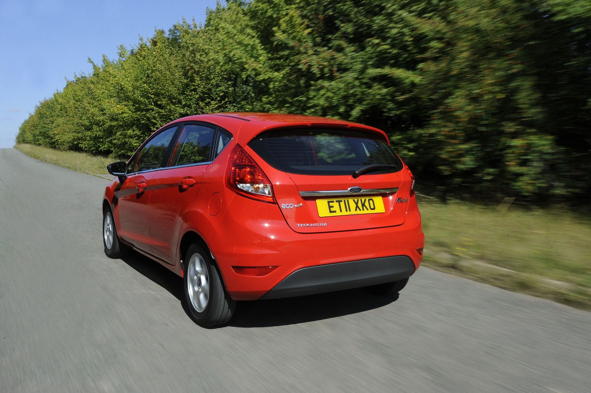 rear view of a red ford fiesta driving down a road with trees on the side