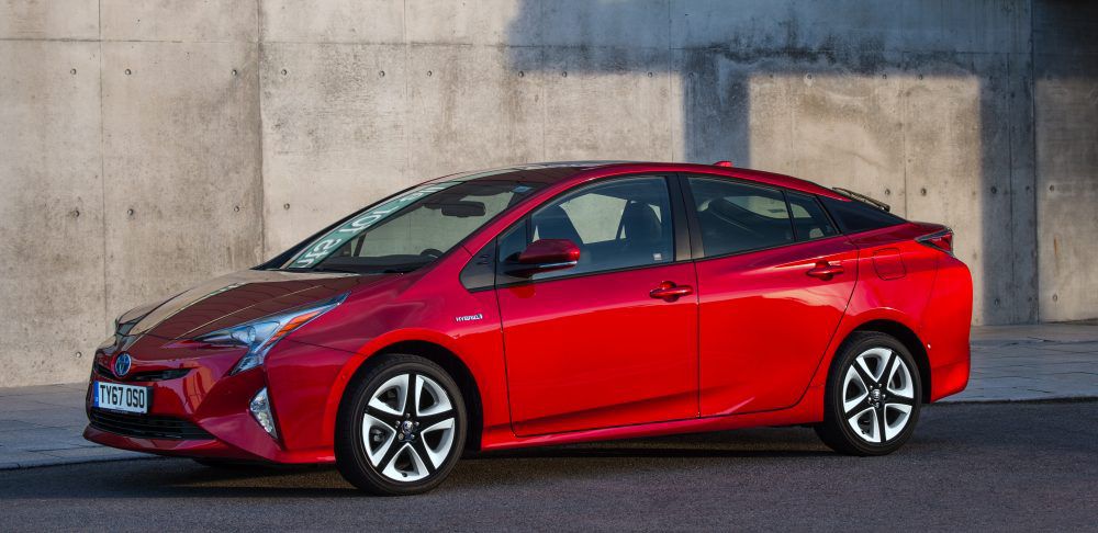 red toyota prius parked next to a concrete wall