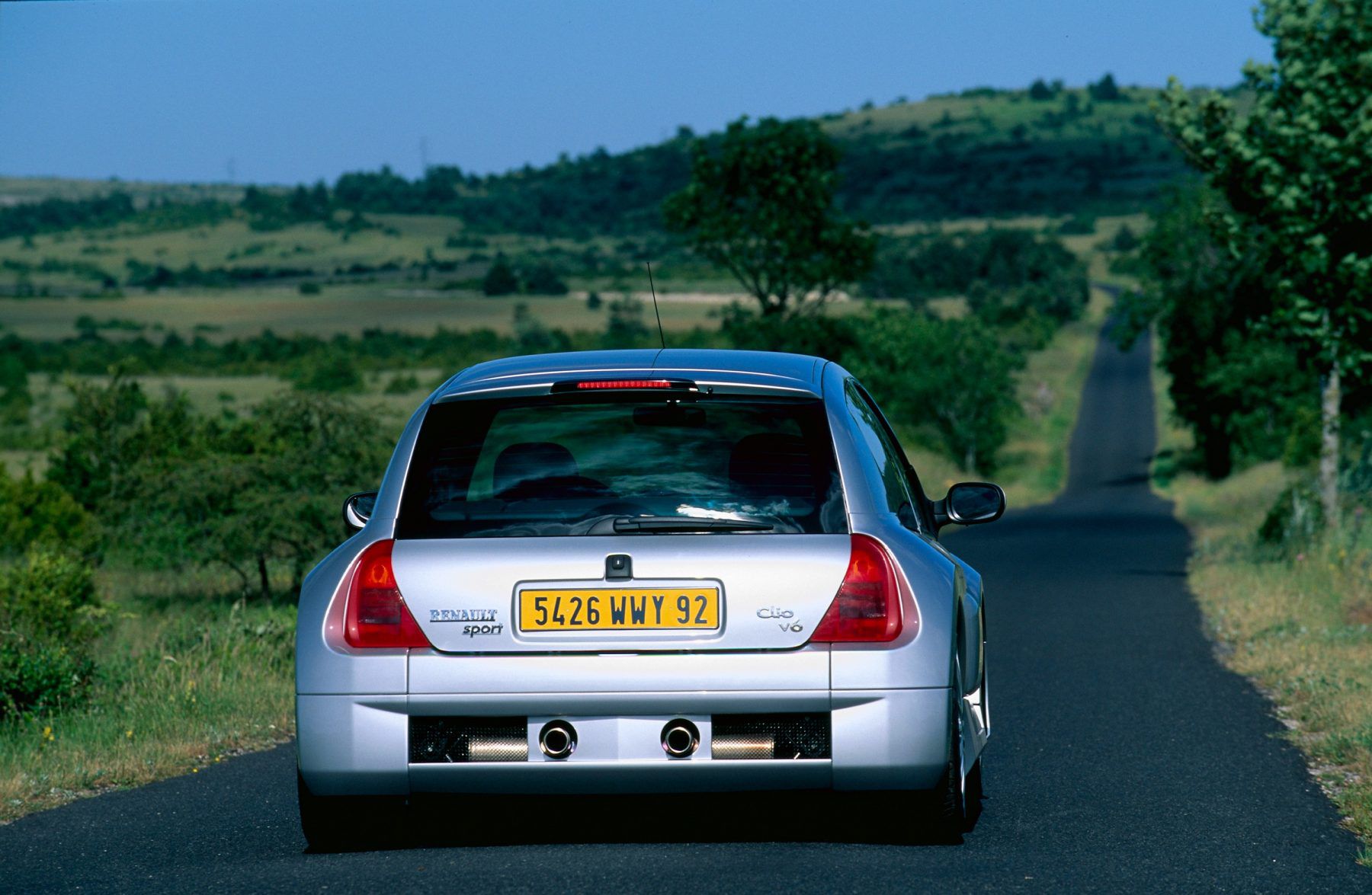 rear view of a renault clio v6 driving down a road