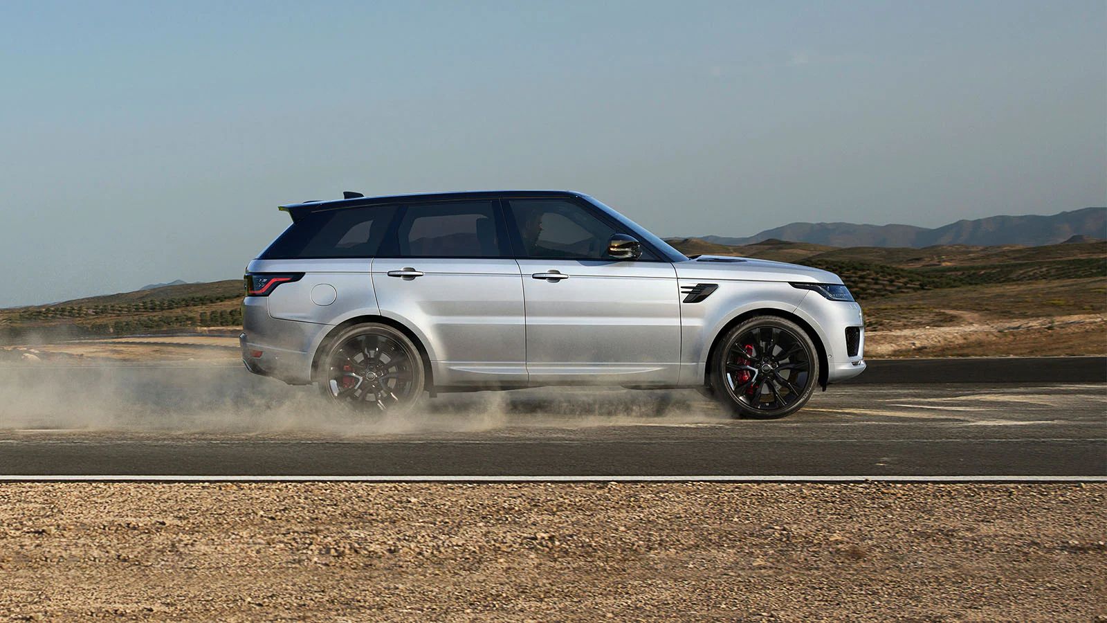 Silver Range Rover Sport side driving down dirt road