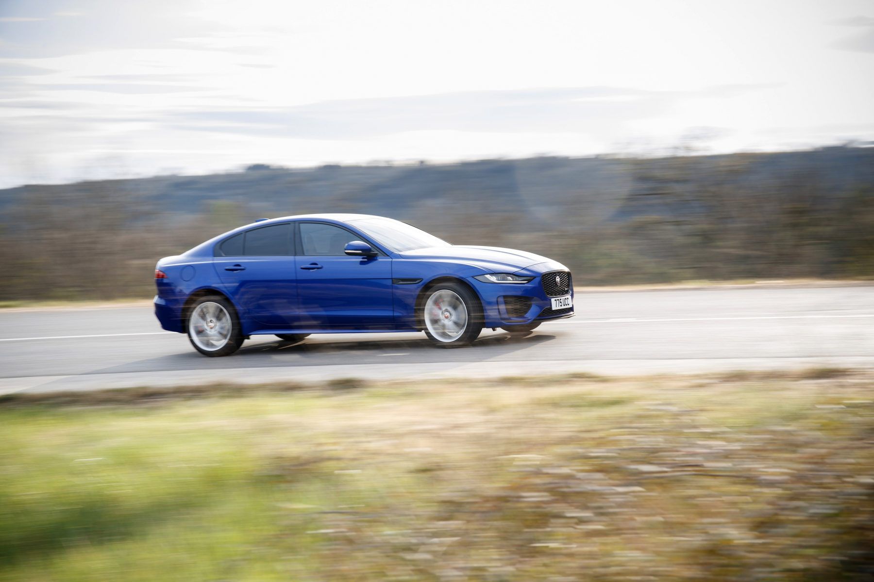 Side View of the blue Jaguar XE driving on a road