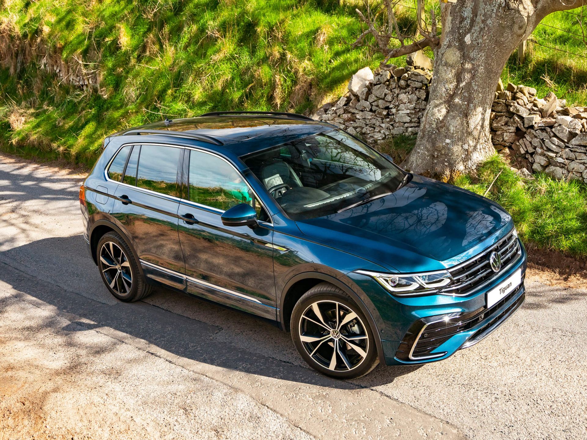 side view of blue volkswagen tiguan with silver alloy wheels parked under a tree