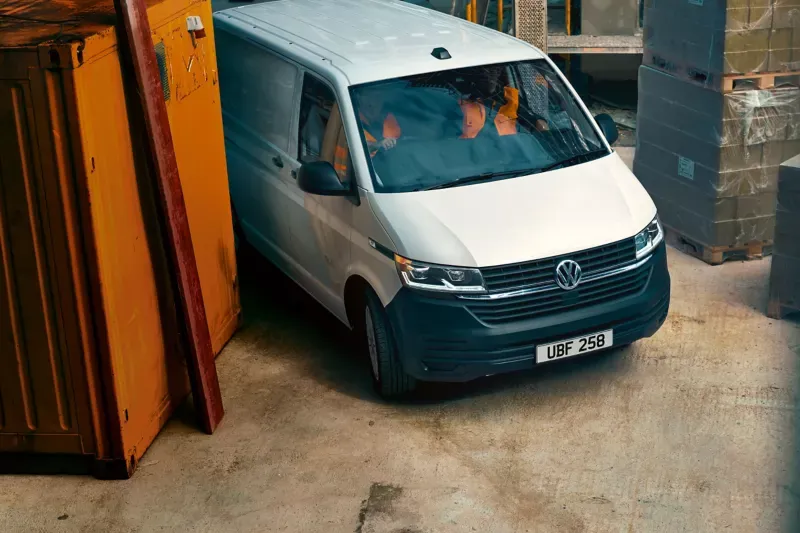 elevated view of white volkswagen transporter panel van being driven by workers