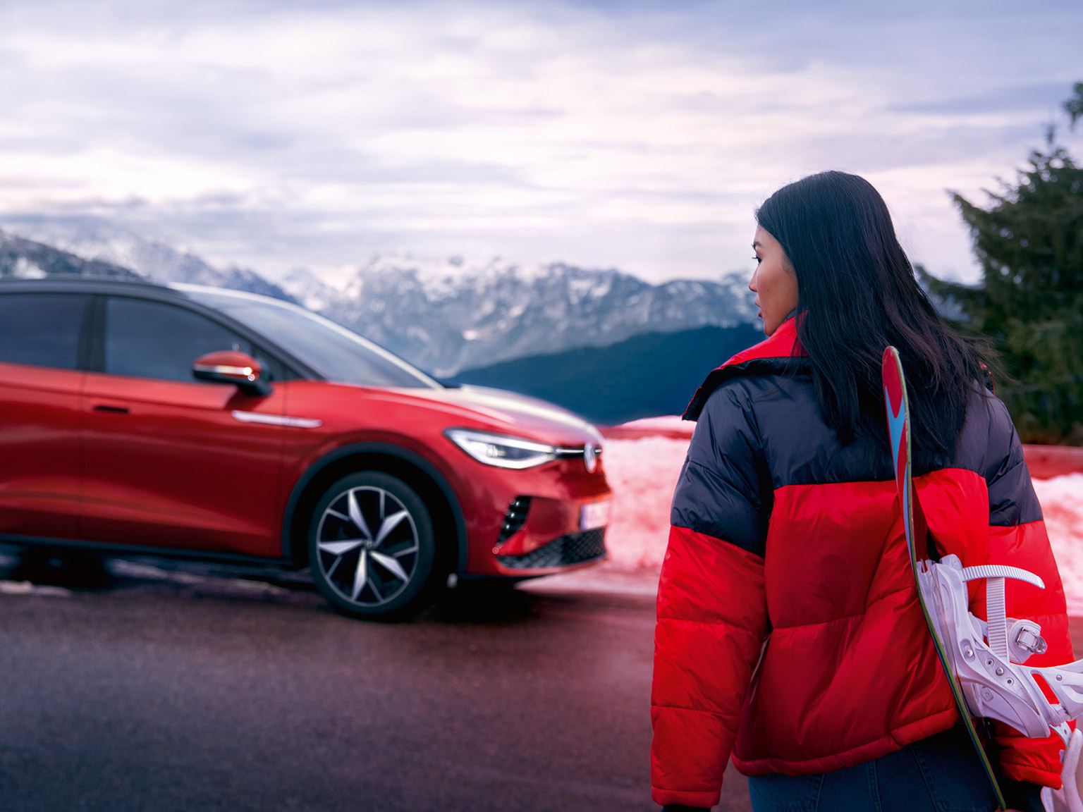 Woman looking at a Red Volkswagen ID4 GTX parked in front of snowy mountains
